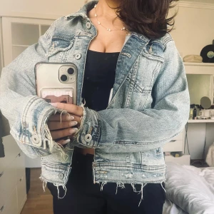  jeansjacka Zara  - Säljer en snygg ljusblå jeansjacka med slitna detaljer och knappar framtill. Jackan har en normal passform och är perfekt för en avslappnad stil. Den är långärmad och har en klassisk krage.