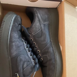 Nike Air Force 1 '07 i mörkblå mocka - Säljer ett par Nike Air Force 1 '07 i en snygg mörkblå färg. Skorna är tillverkade i mocka och har en klassisk design med snörning och rund tå. Perfekta för dig som vill ha en stilren look.