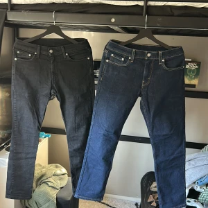 Levi's jeans i svart och blått - Två par Levi's jeans, ett par i svart och ett par i mörkblått. Båda har klassisk femficksdesign och är tillverkade i denim. De blå jeansen är av modellen 511, vilket ger en modern och stilren look.Ett par för 600 eller båda två för 1000kr