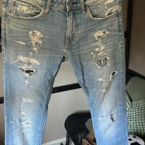 Blå slitna jeans från Crocker - Säljer ett par blå jeans från Crocker med en cool slitningseffekt. De har en klassisk femficksdesign och en knappgylf. Perfekta för en avslappnad stil med en edgy touch.