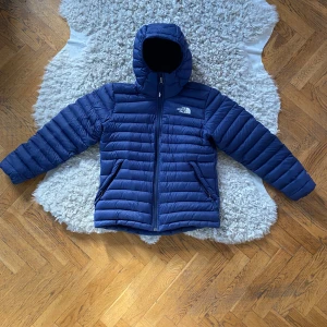 Blå dunjacka från The North Face xs - Säljer en snygg blå dunjacka från The North Face. Jackan har en huva och dragkedja framtill samt två praktiska fickor med dragkedja. Perfekt för kyliga dagar!