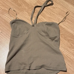 Beige ribbad linnetopp från Gina Tricot - Säljer en stilren beige ribbad linnetopp från Gina Tricot. Toppen har smala axelband och en enkel design som passar perfekt till sommaren. Perfekt för en avslappnad look eller att klä upp med accessoarer.