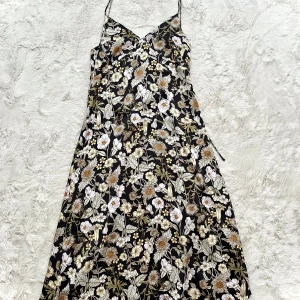 Blommig långklänning med smala axelband - Säljer en vacker långklänning med blommigt mönster i svart, vitt och grönt. Klänningen har smala axelband och en v-ringad design som ger en elegant look. Perfekt för sommarens alla tillfällen!