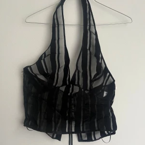 Svart och transparent randig korsett - Snygg svart och transparent korsett med randigt mönster. Den har en djup urringning och snörning framtill för justerbar passform. Perfekt för en kväll ute eller en speciell tillställning.