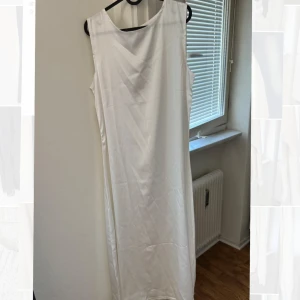 Vit rak  ärmlös långklänning - Elegant vit långklänning med en enkel och stilren design. Klänningen är ärmlös och har en rak passform som ger ett klassiskt intryck. Perfekt för sommarens festligheter eller en stilfull kväll. Passar även bra under en abaya.