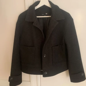 Svart kappa  - Snygg svart kappa med klassisk design. Jackan har stora knappar framtill och praktiska fickor. Perfekt för kyligare dagar med sin stilrena look och bekväma passform.