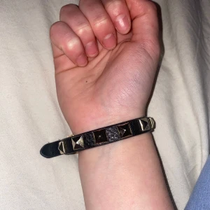 Svart nitarmband - Snyggt svart armband med guldiga nitar. Armbandet har justerbar storlek med flera hål och ett spänne i guld. Säljer då jag inte använder längre. Och jag vet inte vart den kommer från då jag fick den i present 