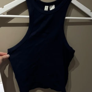 Mörkblå linnetopp från H&M Divided - Säljer en mörkblå linnetopp från H&M Divided. Toppen är ärmlös och har en rund halsringning. Perfekt för varma dagar eller som ett lager under en jacka. Enkel och stilren design som passar till det mesta.