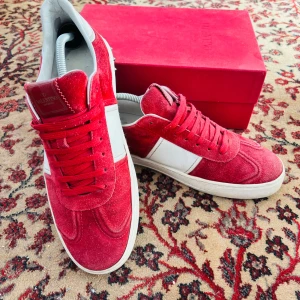 Valentino Flycrew - Snygga röda mockasneakers från Valentino med vita detaljer och snörning. Skorna har en rund tå och en klassisk design som passar perfekt för en stilren look. De kommer i en elegant röd förpackning.