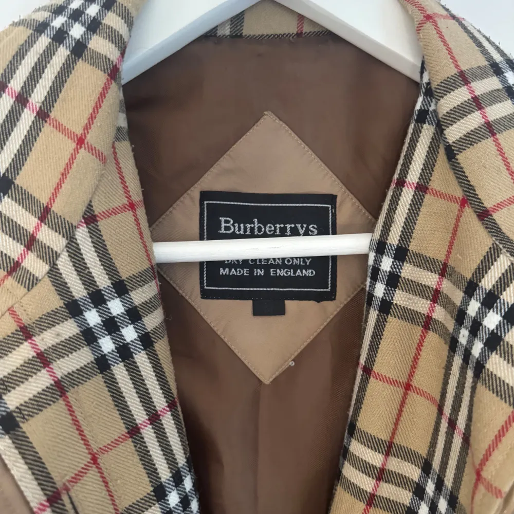 Snygg beige trenchcoat från Burberry med klassiskt rutigt foder. Jackan har ett bälte i midjan och långa ärmar. Perfekt för en stilren look, dock lite fläckar. Men har inte försökt tvätta bort dem.. Takit.