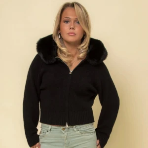 Svart cardigan jacka med fuskpäls - Mysig svart cardigan jacka med dragkedja och bred krage i fuskpäls. Jackan är croppad med ribbade muddar och har en clean look som passar till jeans eller kjol. Perfekt för dig som gillar en stilren vibe med lite extra fluff vid kragen.