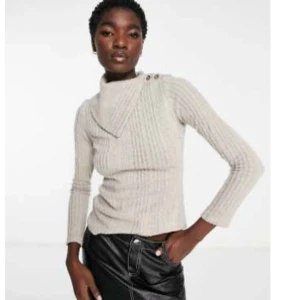 Beige ribbad tröja med knappar och rullad krage  - Säljer en stilren beige ribbad tröja med unik krage och knapplösning vid axeln. Köpt från ASOS, märke River Island. 94% Polyester och 6% elasten. Storlek 40. Endast använd ett fåtal antal gånger 🩷
