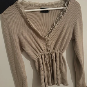 Beige ribbad kofta från Soaked in Luxury -  beige ribbad kofta från Soaked in Luxury. Den har långa ärmar och spetsdetaljer vid halsringningen. Tröjan har en knytning framtill. De står storlek L på tröjan men skulle säga att den är mer en s/m då man knyter i midjan så de blir ”tajtare” nypris 800kr