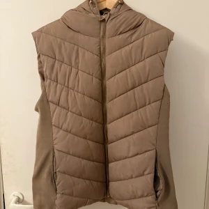 Beige väst från Zara - Hej! Säljer en snygg beige väst från Zara med dragkedja och huva. Västen har ett quiltat mönster och är perfekt för vår/höst dagar. Den är både stilren och praktisk med sina sidofickor.