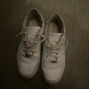 Vita sneakers från Nike - Klassiska vita sneakers från Nike med snörning och rund tå. Perfekta för en avslappnad stil och passar till det mesta. Sula med bra grepp och ikonisk design.