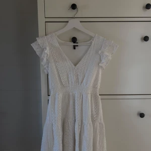 Vit spetsklänning med volangärmar - Superfin vit kortklänning från VERO MODA med v-ringning, volangärmar och broderade spetsdetaljer. Klänningen har smock i midjan och är perfekt för sommarens alla tillfällen. Använd 1 gång och är i helt nytt skick.