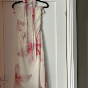 Midi scarf dress Gina Tricot -  Supersnygg vit långklänning med stora rosa liljor. Klänningen är axelbandslös och har figurnära passform samt en lång scarf! Tunt, flowy material som känns lyxigt och somrigt. (Storlek M men passar också mig som normalt är xs/s, väldigt stretchigt material.)  Endast använd en gång, ordinarie pris 599 💗
