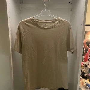 Beige t-shirt  - Enkel och stilren beige t-shirt från SOC i mjuk bomull. Klassisk rund halsringning och korta ärmar, perfekt för en clean och avslappnad look. Passar dig som gillar basic och neutrala färger. Storek m. Knappt använd