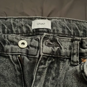 Svarta wide jeans från Grunt - Säljer ett par svarta jeans från Grunt med snygg tvättad look. Jeansen har raka, vida ben och klassisk femficksdesign. De är tillverkade i jeansmaterial och har dragkedja och knapp framtill. Perfekta för en avslappnad och trendig stil.