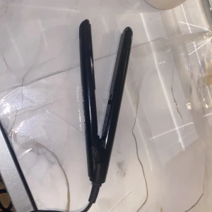 Svart plattång från Beautine - Säljer en stilren svart plattång från Beautine. Den har en smal och slät design med keramiska plattor och lång sladd, perfekt för att styla håret snabbt och enkelt. Passar både till att platta och skapa lockar. Enkel att använda och smidig att ta med.