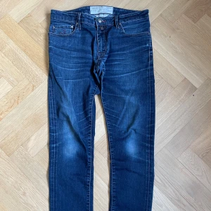 Blå Jacob cohën jeans - Mörkblåa slim fit Jacob cohens med fadings på fram och baksida, står stl 33, skulle säga att det känns som 32x 30. Exakta mått är: totallängd 98cm, innersöm 77cm, midja (bälteshölla-bälteshölla) 40cm 