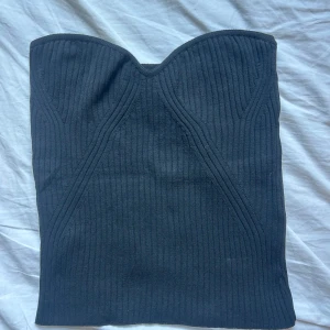 Svart ribbad tubtopp från Lindex - Säljer en svart ribbad tubtopp från Lindex i storlek S. Toppen har en bandeauformad överdel med markerad byst och är helt ärmlös. Materialet är stretchigt och sitter tight mot kroppen. Aldrig använd