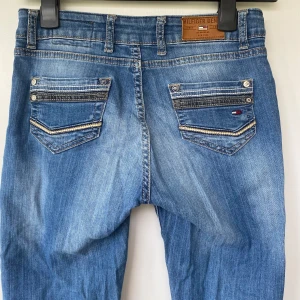Blå jeans från Tommy Hilfiger - Snygga blå jeans från Tommy Hilfiger med klassisk femficksdesign och kontrastsömmar. Jeansen har raka ben, normal passform och detaljerade bakfickor med Hilfiger-logga. Tillverkade i mjukt denimtyg som ger en avslappnad look.