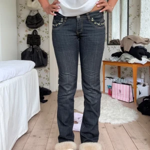 Mörka bootcut jeans med detaljer - Snygga mörkgrå jeans med bootcut passform och coola detaljer som nitar och broderier på fickorna. Jeansen har kontrastsömmar och sitter tajt upptill med utsvängda ben. Perfekta för dig som gillar en trendig och unik look.
