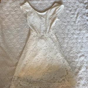 Vit spetsklänning med omlott  - Superfin vit kortklänning i spets med omlottdetalj och cutout i midjan. Klänningen har korta ärmar och vacker blommig spets över hela plagget samt en söt kant nertill💗