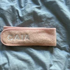 Rosa smink band  från CAIA - Säljer ett mjukt och praktiskt rosa diadem från CAIA i frotté med broderad logga framtill. Perfekt när du vill hålla håret borta vid sminkning eller hudvård. Justerbar med kardborre för bästa passform.