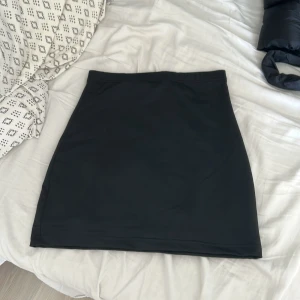 Svart kortkjol i enkel stil - Enkel och stilren svart kortkjol med rak passform. Kjolen är helfärgad utan detaljer och passar perfekt till en basic eller dressad look. Materialet känns mjukt och följsamt, vilket gör den bekväm att bära hela dagen.