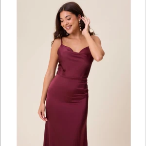 Vinröd långklänning från Bubble Room - Supersnygg vinröd långklänning med tunna axelband och draperad urringning. Klänningen har en figurnära passform och är gjord i ett glansigt, satinliknande material. Perfekt för dig som vill sticka ut med en elegant och trendig look. Den är aldrig använd vilket man kan se på prislapparna som hänger kvar! Säljer pga att jag inte hann skicka tillbaka den då jag råkade köpa hem 2 lika dana!