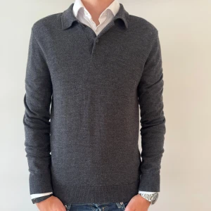 MORRIS MERINOULL TRÖJA  - Snygg mörkgrå stickad pikétröja från Morris med klassisk krage och knappslå. Tröjan är långärmad och har en clean, tidlös look som passar perfekt till jeans eller chinos. Materialet är mjukt och ger en skön känsla hela dagen.