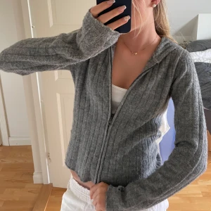 Grå ribbad hoodie med dragkedja - Mysig grå hoodie från 157 med ribbad struktur och dragkedja framtill. Tröjan har huva, långa ärmar och är stickad i ett mjukt material som passar perfekt till chill dagar. Enkel att matcha med både jeans och mjukisbyxor.