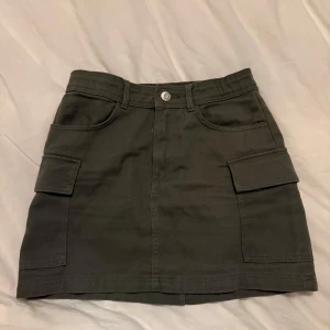 Mörkgrön cargokjol med fickor - Grön jeanskjol med fickor framtill. Färgen är lite mer grön i verkligheten. Endast använd någon gång. Storlek 146 men passar mig som brukar ha xxs-xs