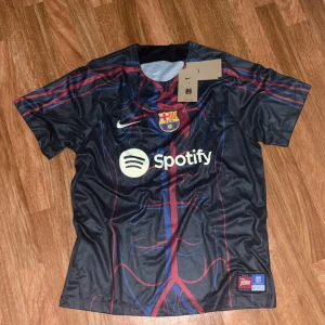 FC Barcelona Nike fotbollströja M - FC Barcelona matchtröja från Nike med Spotify-logga på bröstet. Tröjan är svart med röda och blå detaljer, klubbmärke och Nike Swoosh. Tillverkad i Dri-FIT-material som andas, perfekt för fotboll eller träning. Kortärmad och med modern design.