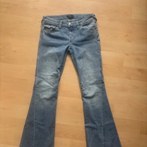 True Religion Joey Low Rise Flare Jeans - Snygga ljusblå jeans från True Religion, modell Joey Low Rise Flare. De är storlek W27. Det är en liten reva högst upp på baksidan av jeansen, se bild. De är knappat använda.