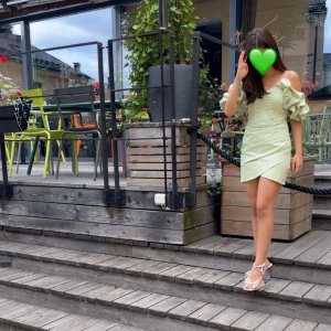 Ljusgrön kort klänning med volangärm - Superfin ljusgrön kort klänning med offshoulder och volangärmar. Klänningen har en omlottkjol och markerad midja som ger en snygg siluett. Perfekt för dig som vill sticka ut med en trendig och feminin look.