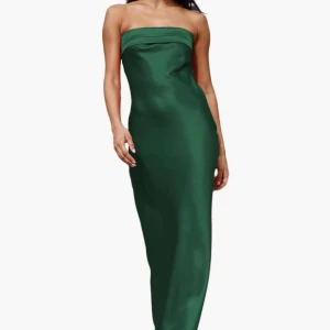 Grön axelbandslös långklänning - Snygg grön axelbandslös långklänning i satinliknande material. Klänningen har en rak, figurnära passform och öppen rygg med cool detalj. Perfekt för dig som vill sticka ut med en elegant och modern look.
