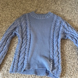 Ljusblå stickad tröja Gina Tricot - Supersöt ljusblå stickad tröja från Gina Tricot i storlek XS. Tröjan har grovstickat mönster med snygga flätor längs ärmar och sidor, samt ribbad halsringning och muddar. Perfekt för lager-på-lager och chill dagar.