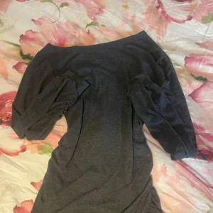 Mörkgrå offshoulder klänning/ Tröja - Snygg mörkgrå kortklänning med offshoulder-modell och trekvartsärmar. Klänningen har rynkade detaljer vid ärmar och ena sidan, vilket ger en cool och trendig look. Mjuk och stretchig bomullskänsla, perfekt för dig som gillar stilrena plagg med twist.