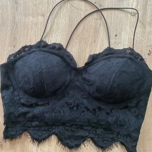 Svart spetskorsett från NLY One - Supersnygg svart korsett-topp från NLY One med tunna axelband och vadderade kupor. Toppens spetsdetaljer och vågig kant ger en extra touch. 