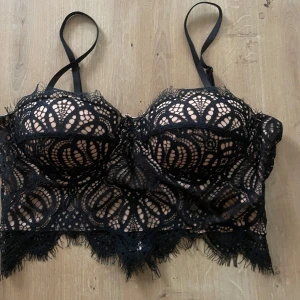 Svart spetskorsett från Amisu - Supersnygg svart korsett från Amisu med spetsdetaljer och vadderade kupor. Toppen har justerbara axelband, dragkedja bak och fransig spetskant nertill. Aldrig använd, lapp kvar.