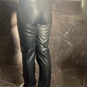 Svarta raka byxor i skinnimitation - Snygga svarta byxor i skinnimitation med raka ben och klassisk femficksdesign. Byxorna har hög midja och stängs med dragkedja och knapp. Perfekta för dig som vill ha en edgy look med stilren vibe. Dem är från lager 157 i modellen icon. Säljer pga att det inte används. Mid waist.