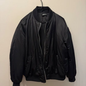 Svart bomberjacka från Gina Tricot oversized - Säljer en svart bomberjacka från Gina Tricot med klassisk ribbad krage, muddar och dragkedja framtill. Jackan har en loose passform och är tillverkad i ett glansigt syntetmaterial. Perfekt för dig som gillar en clean och stilren look. Storlek xs men är oversized, jag har i vanliga fall S/M.