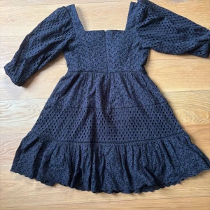 Svart kortklänning By Malina - Supersöt svart kortklänning från By Malina med broderade hål, volangkant och trekvartsärmar. Klänningen har fyrkantig ringning och dragkedja i ryggen. Använd 2 ggr. 