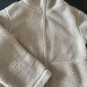 Beige teddyjacka från lager 157 - Mysig beige teddyjacka från 157 i storlek XS. Jackan har dragkedja framtill, huva och är tillverkad i fluffigt teddy-material som håller dig varm. Perfekt för kyliga dagar när du vill ha en chill och avslappnad stil. Pris går att diskutera!