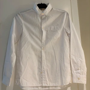 Vit skjorta från H&M, strl 158 - Klassisk vit skjorta från H&M i storlek 158. Skjortan har lång ärm, bröstficka och knäppning framtill. Tillverkad i bomull och enkel att stryka tack vare easy iron-tyget. Perfekt för dig som vill ha en stilren och enkel look.