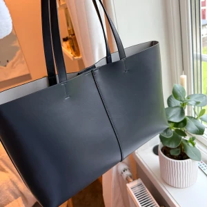 Mörkblå shoppingväska  - Stilren mörkblå shoppingväska. Den är rymlig med ljus insida och magnetknäppning. Perfekt för att bära med sig allt man behöver till vardagen. Enkel och klassisk look som passar till många outfits.