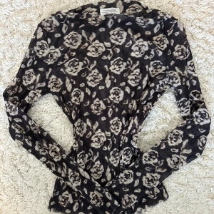 Svart blommig mesh topp från &OtherStories  - Säljer en svart mesh topp från &OtherStories med beige blommigt mönster. Toppen är tight och har långa ärmar samt en lätt ribbad struktur. Perfekt att styla lager på lager eller som statement piece.